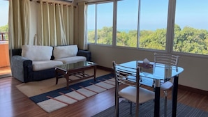 A room with a sofa, a glass table, and a chair, with a view of greenery outside. - Thipurai Beach Hotel (Hua Hin)