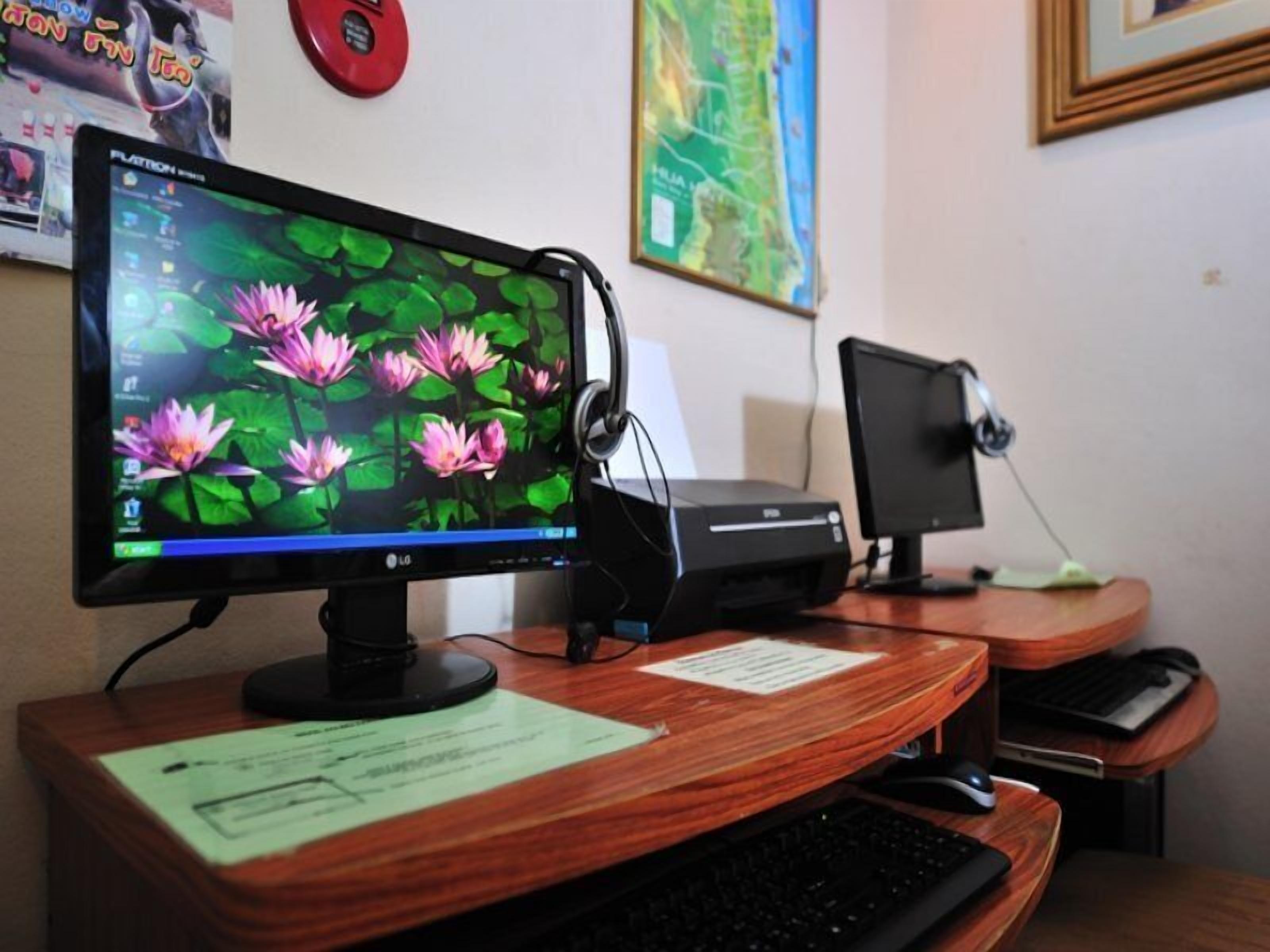 A desk with a computer monitor displaying a wallpaper of pink flowers, a printer, and a keyboard.