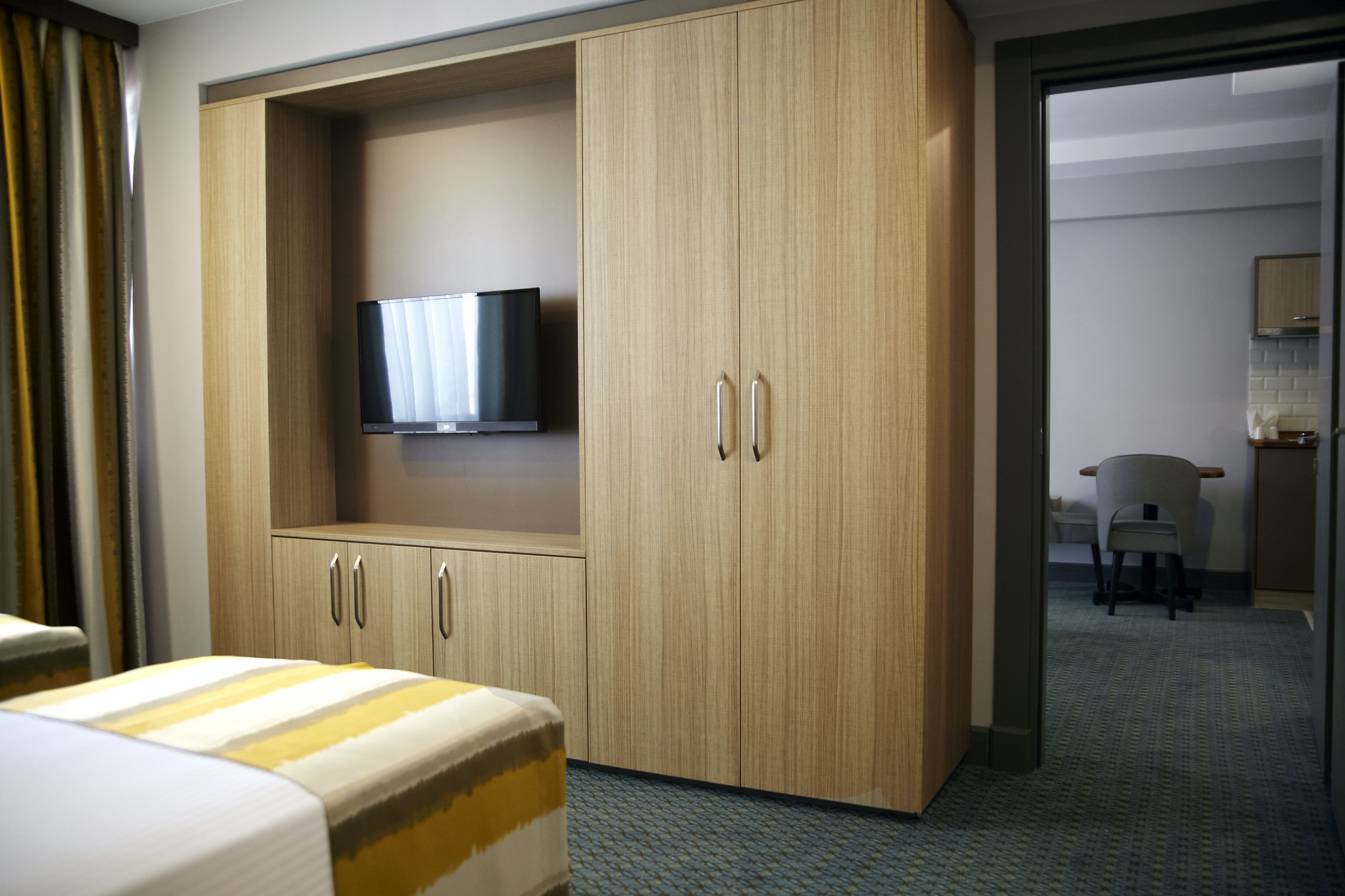 Ein Hotelzimmer mit großem Kleiderschrank, Flachbildfernseher, Bett und einer kleinen Arbeitsfläche.