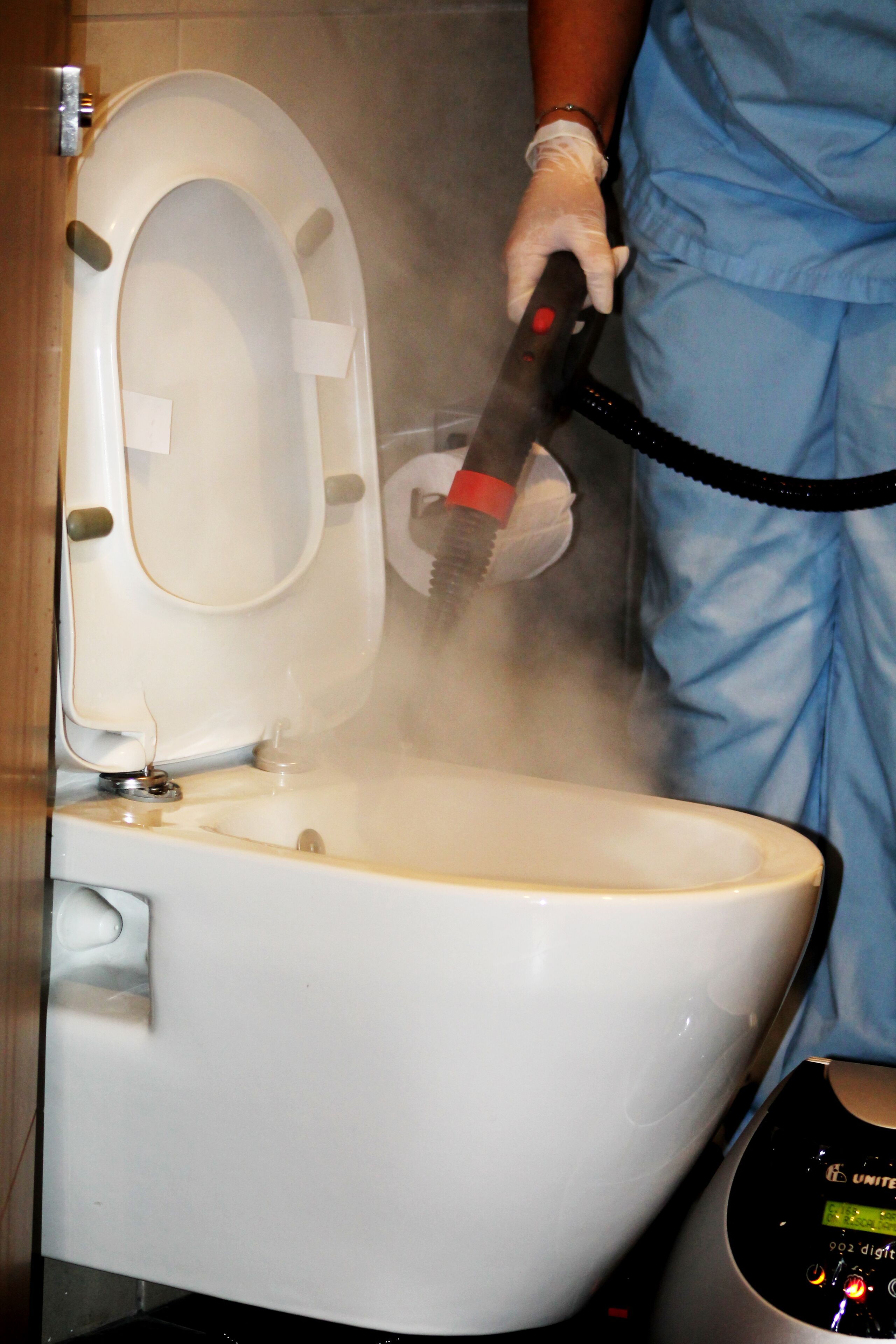 A toilet being cleaned with a steam cleaner.