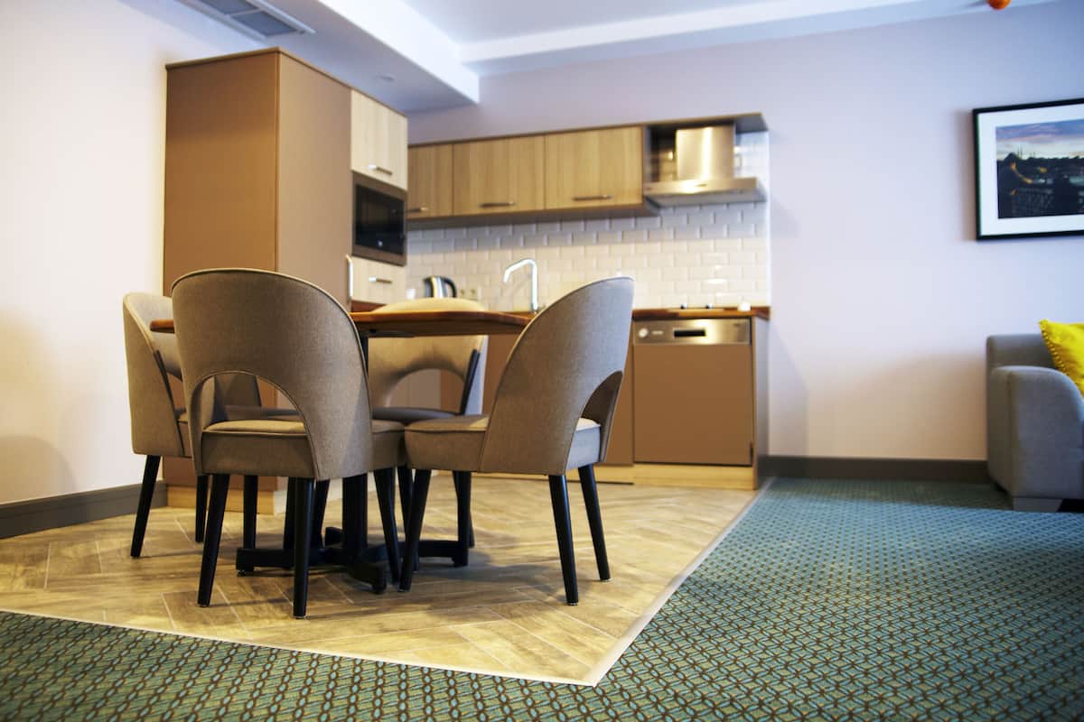 A modern kitchen with wooden cabinets, a built-in oven, and a dining area with four chairs.