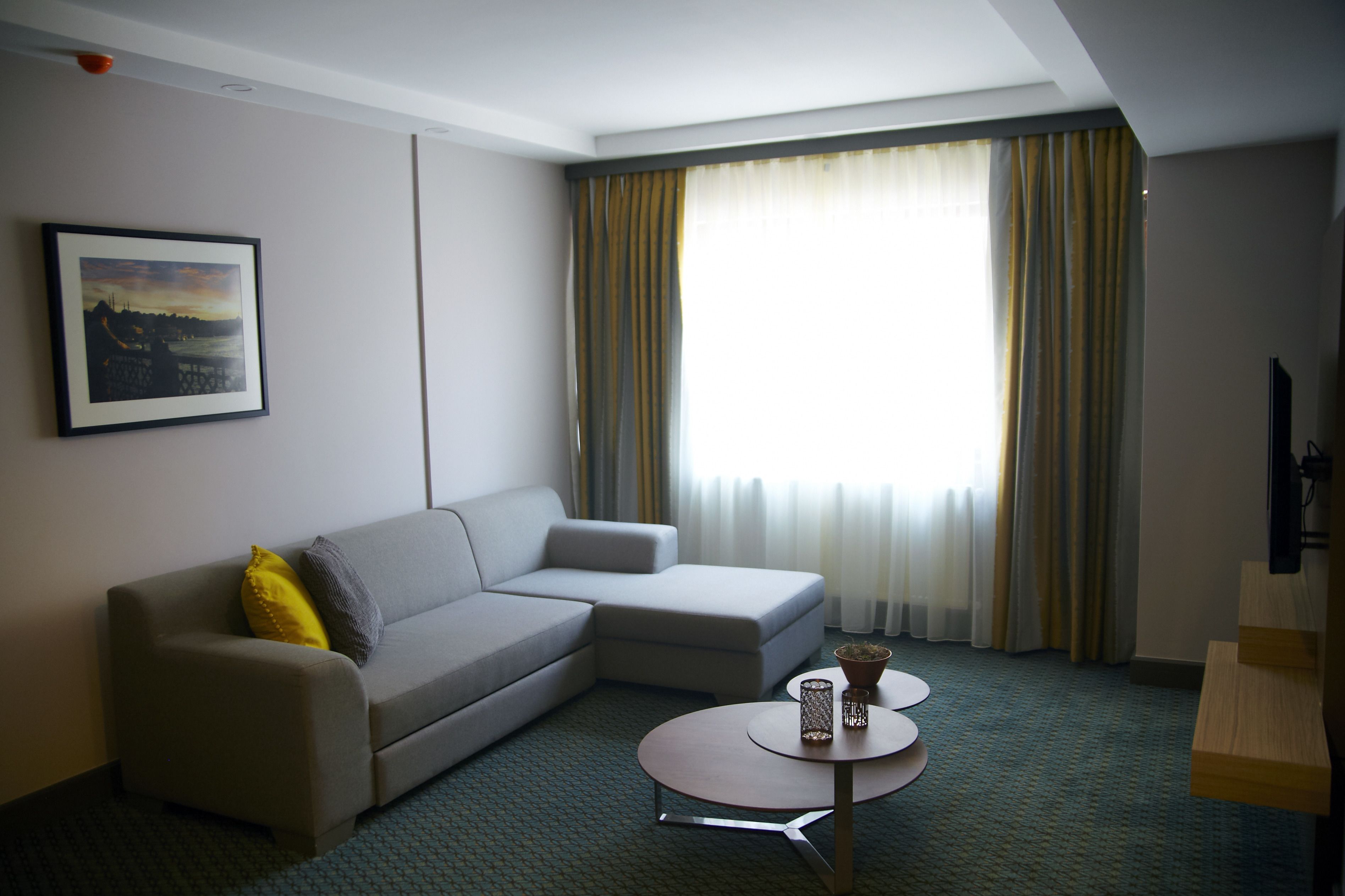 A hotel room with a grey sofa, a small table with a vase, and a framed picture on the wall.