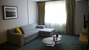A hotel room with a grey sofa, a small table with a vase, and a framed picture on the wall.