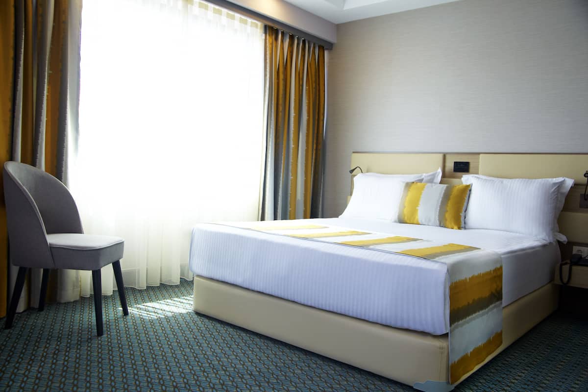 A hotel room with a large bed, a chair, and curtains.