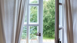 Una habitación con un ventanal amplio, cortinas blancas y dos lámparas fijadas a la pared.