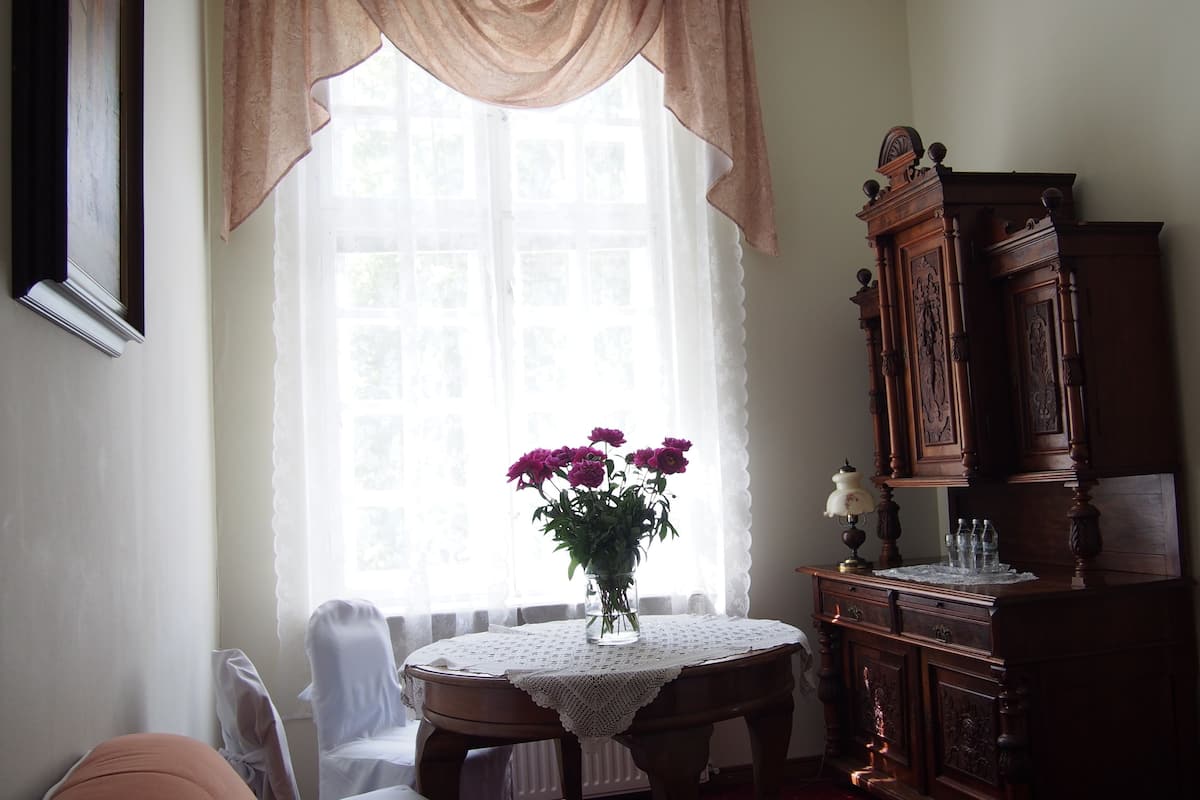 Una habitación con una mesa, sillas, un armario de madera y una ventana con cortinas.