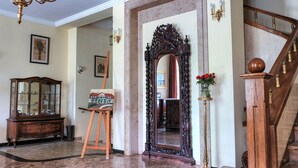 Un amplio pasillo con un espejo grande, una escalera de madera y un candelabro.