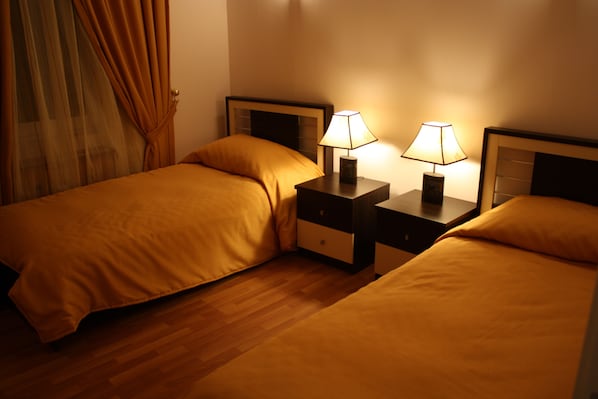 A hotel room with two beds, wooden flooring, and bedside lamps.