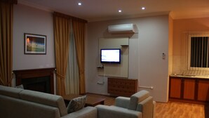 A living room with a fireplace, a television, and a kitchen area. - Qafqaz Sahil Resort Hotel (Lankaran)