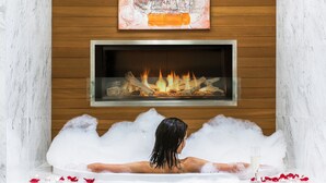 Un cuarto de spa con suelo de mármol, chimenea y una persona relajándose en una bañera llena de burbujas.