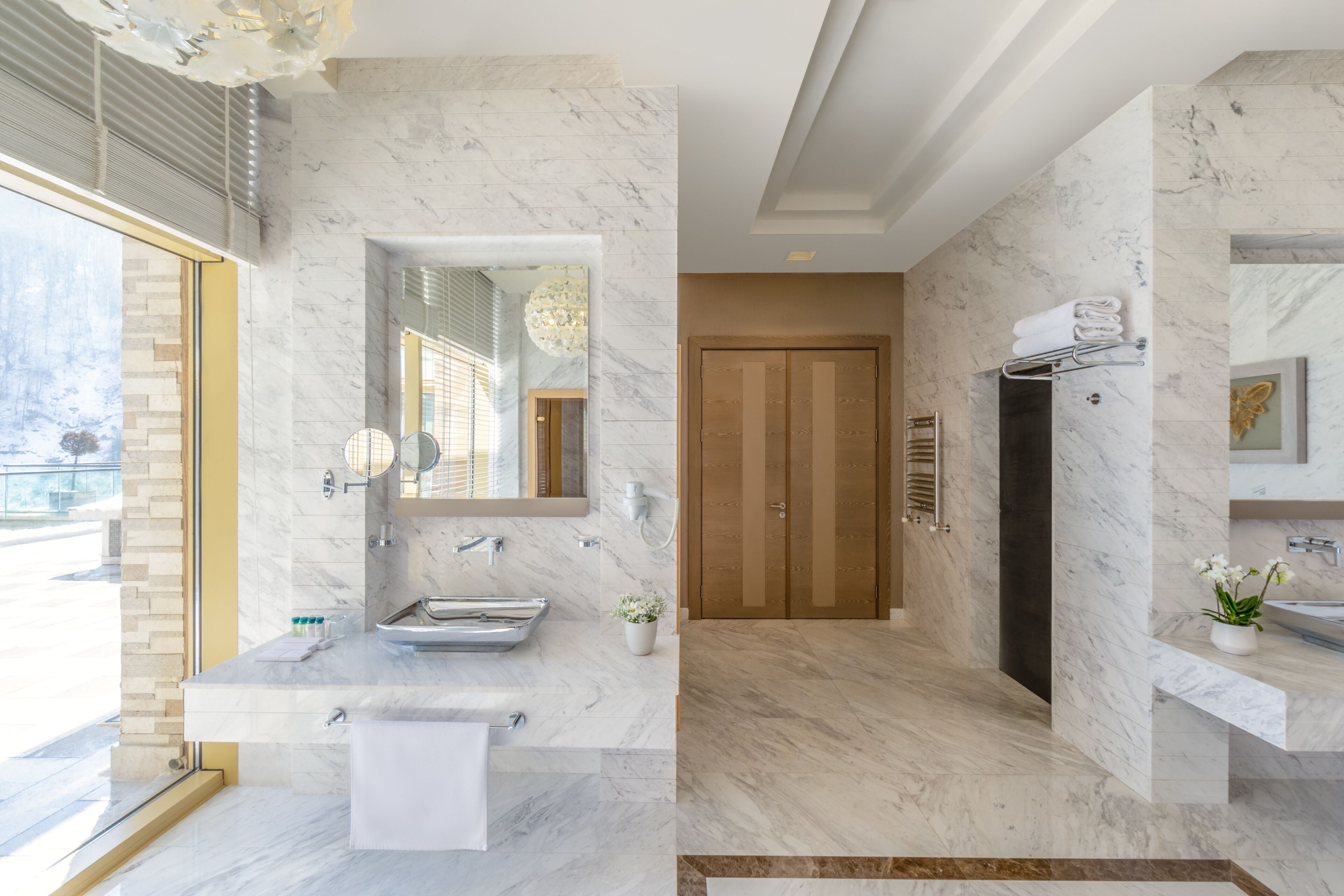 Un baño moderno con encimeras de mármol, un espejo grande y una puerta de madera.
