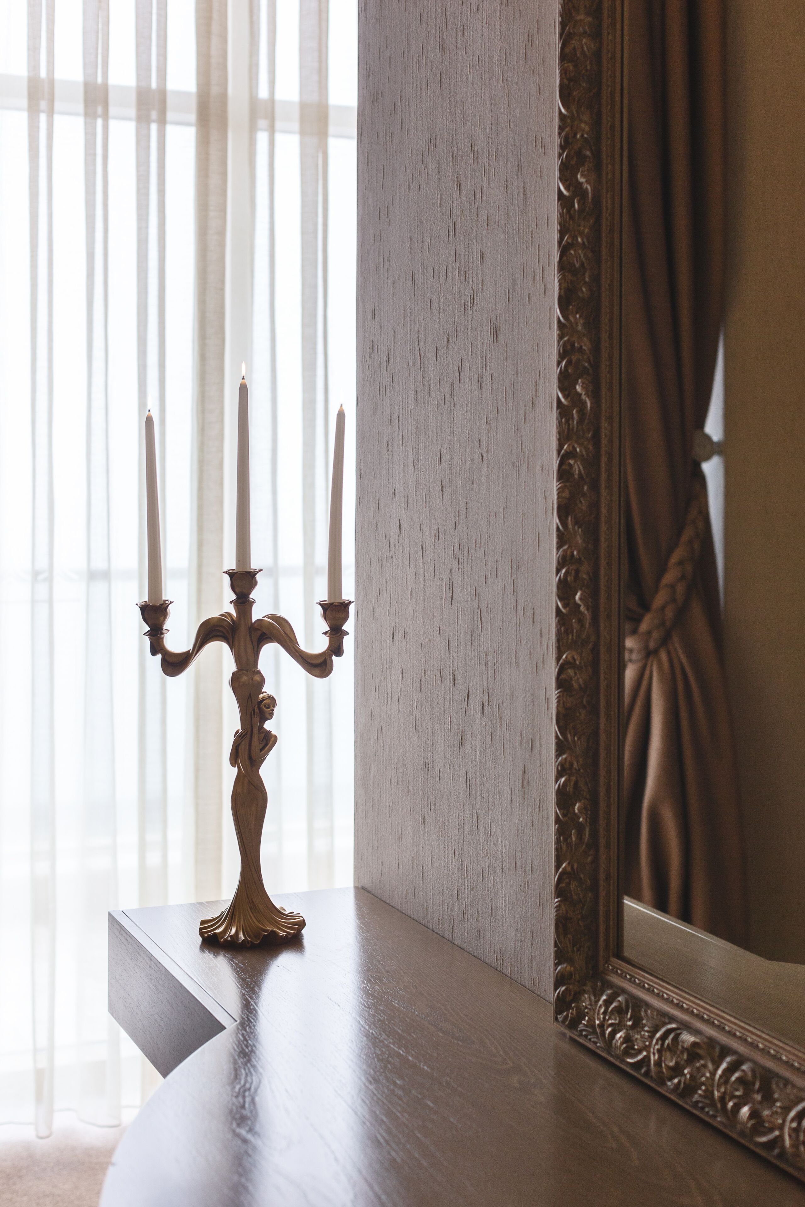 A candelabra with three candles on a wooden table next to a mirror with an ornate frame.