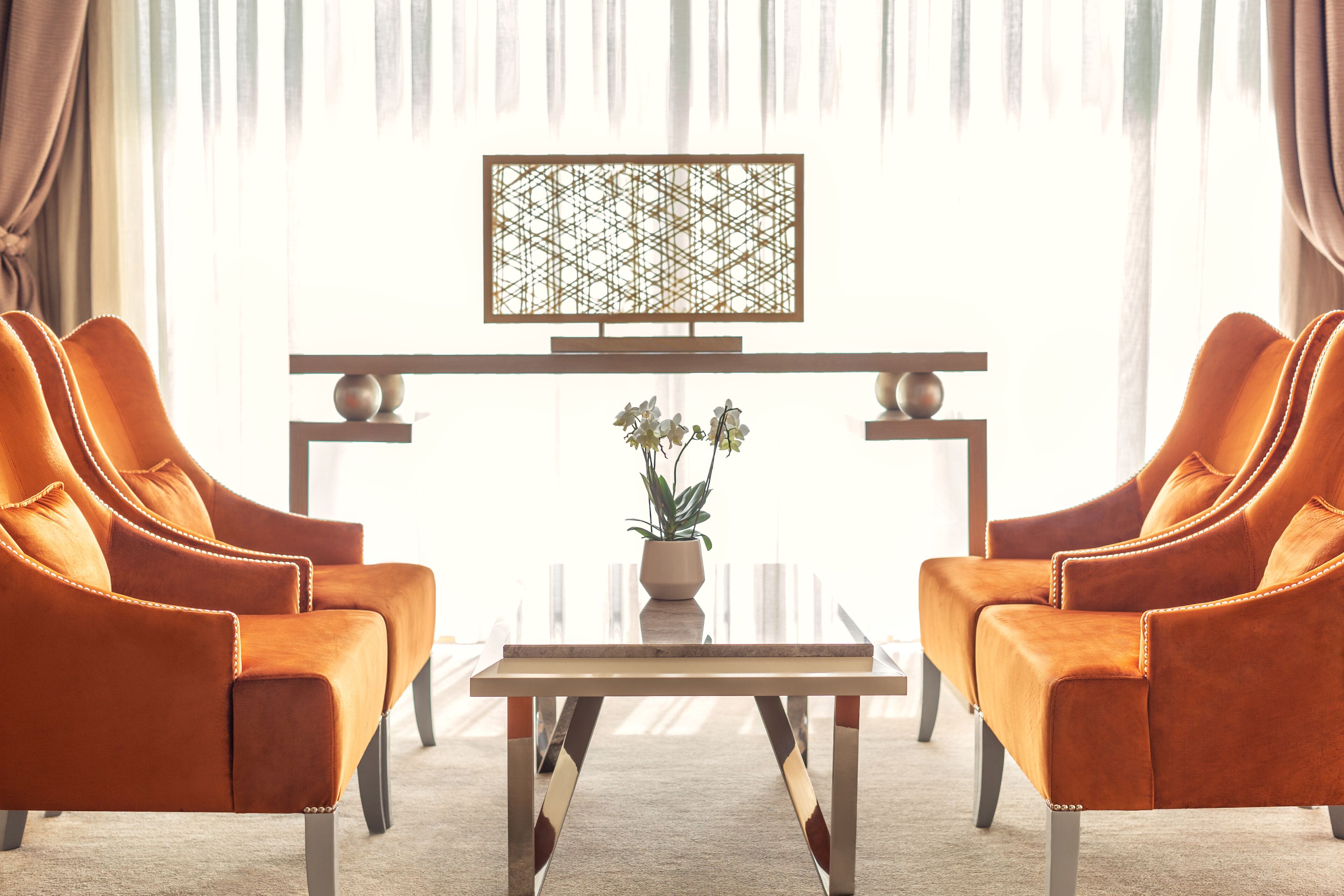 A room with two orange armchairs, a small table, and a decorative screen.