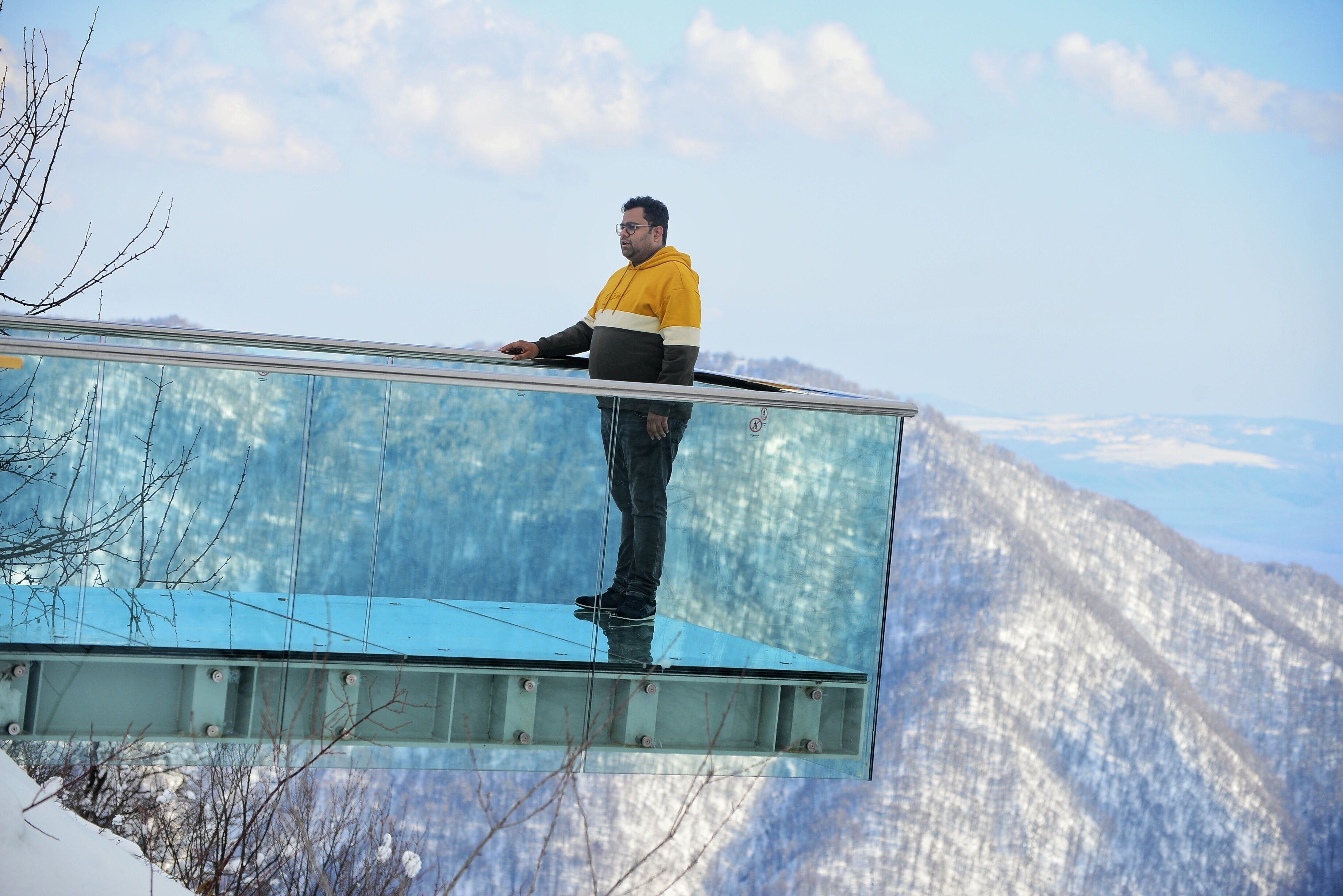 Una persona de pie sobre un puente de cristal, con un paisaje montañoso al fondo.