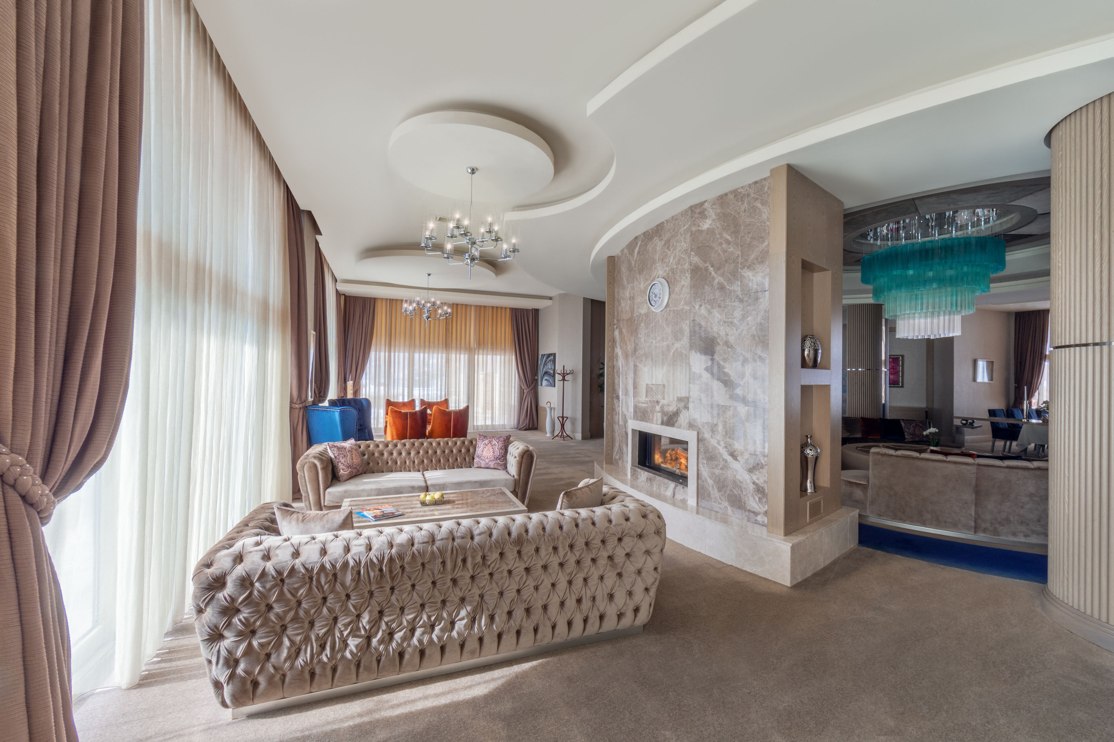 A spacious living room with a large tufted sofa, a fireplace, and a modern chandelier.