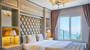 Un dormitorio amplio con una cama grande, un cabecero capitonado, lámparas de noche y vistas al exterior.