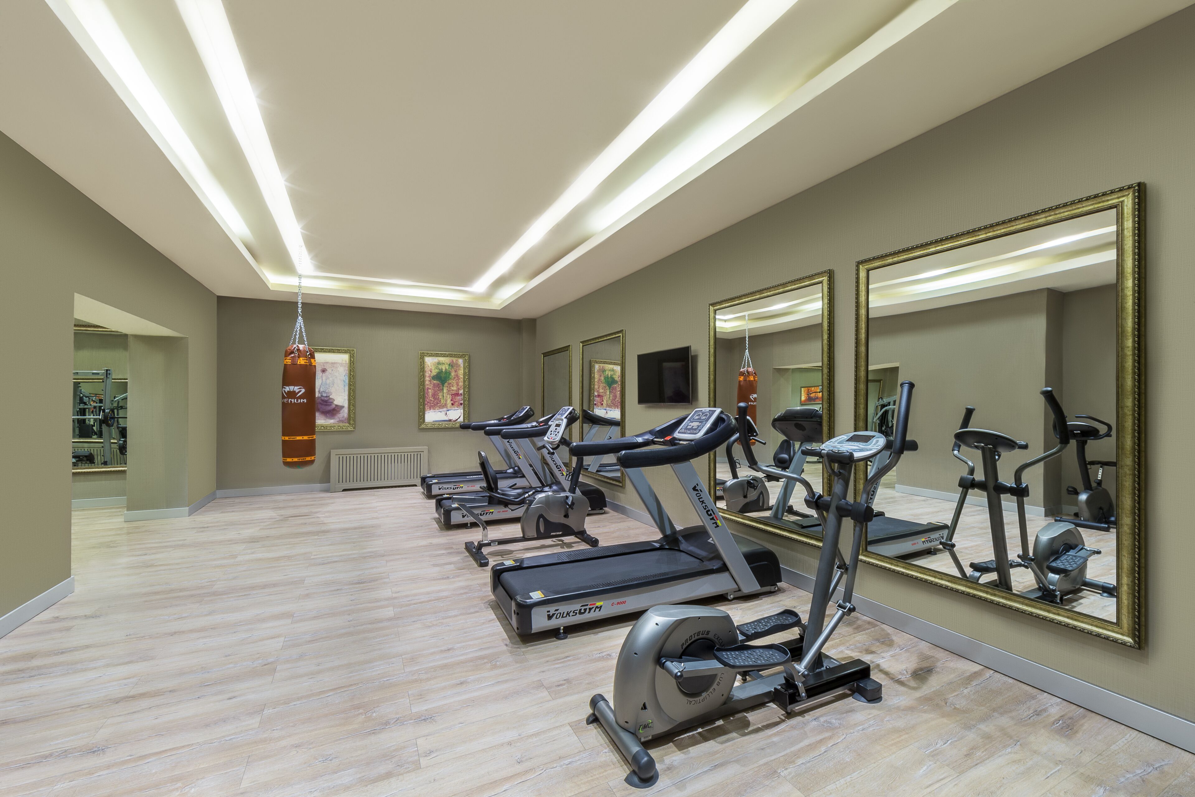 Une salle de sport équipée de tapis de course, d’elliptiques et de vélos d’appartement, avec des miroirs aux murs et un sac de frappe.