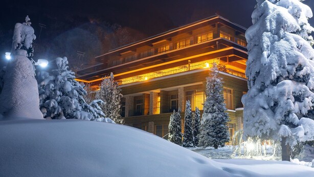 Un hotel con una estructura de varios pisos, balcones iluminados y un entorno cubierto de nieve.