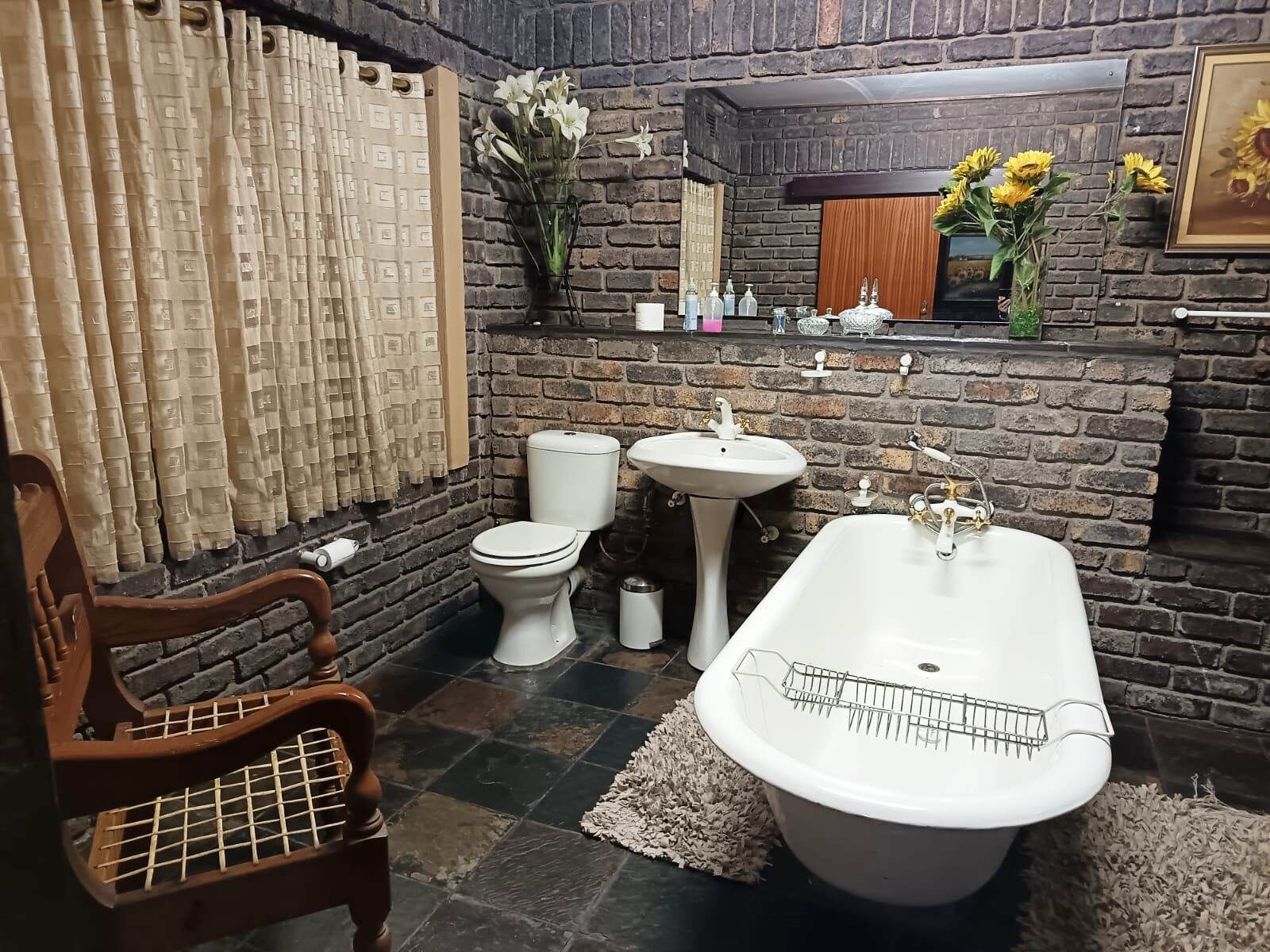 A bathroom with a brick wall, a white toilet, a pedestal sink, and a freestanding bathtub.