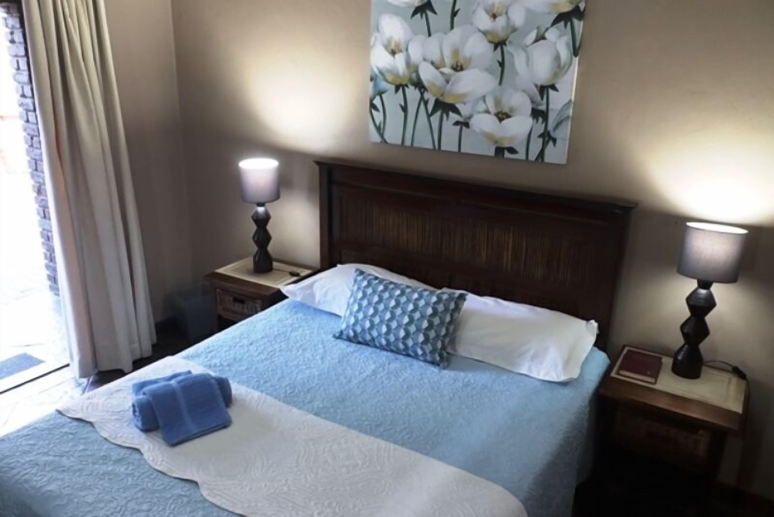 A hotel room with a large bed, two bedside tables with lamps, a painting on the wall, and a window with curtains.