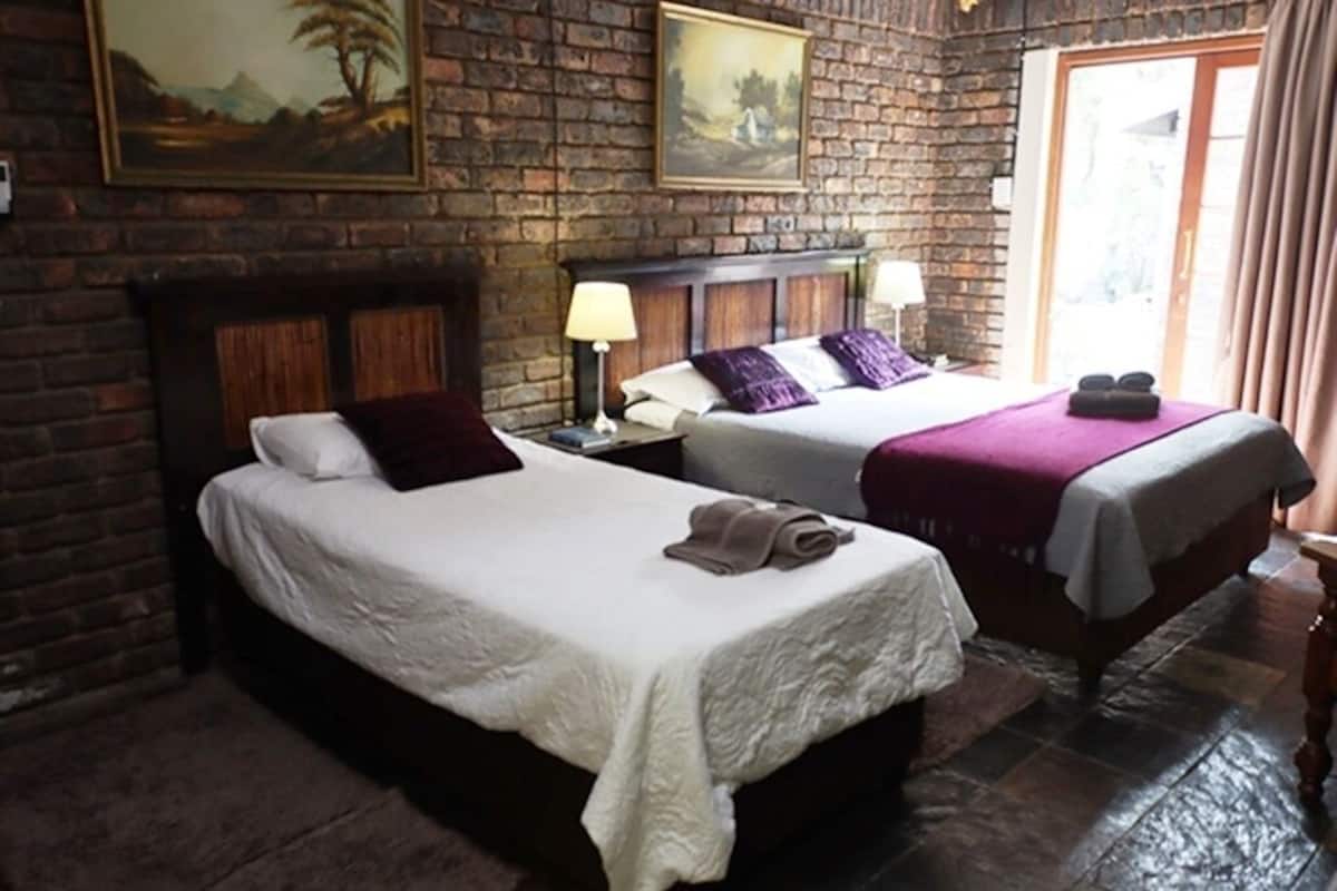 A room with two beds, a brick wall, and a large window with curtains.