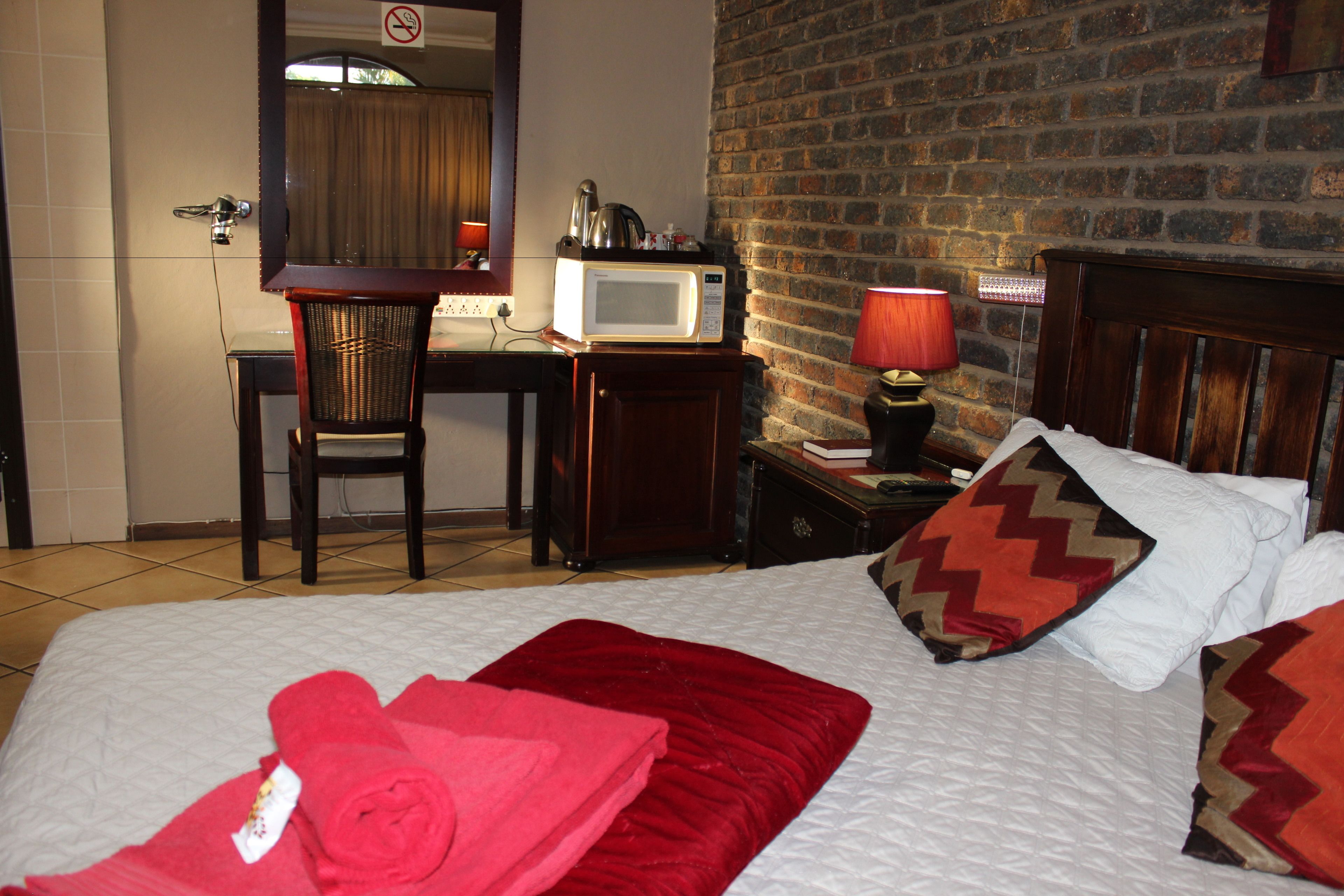Une chambre d’hôtel avec un lit, un bureau avec un ordinateur, une chaise, un four à micro-ondes et un mur en briques.