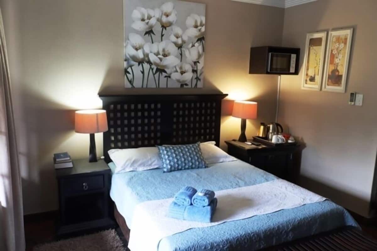 A hotel room with a bed, two bedside lamps, a nightstand, a wall-mounted TV, and a painting.