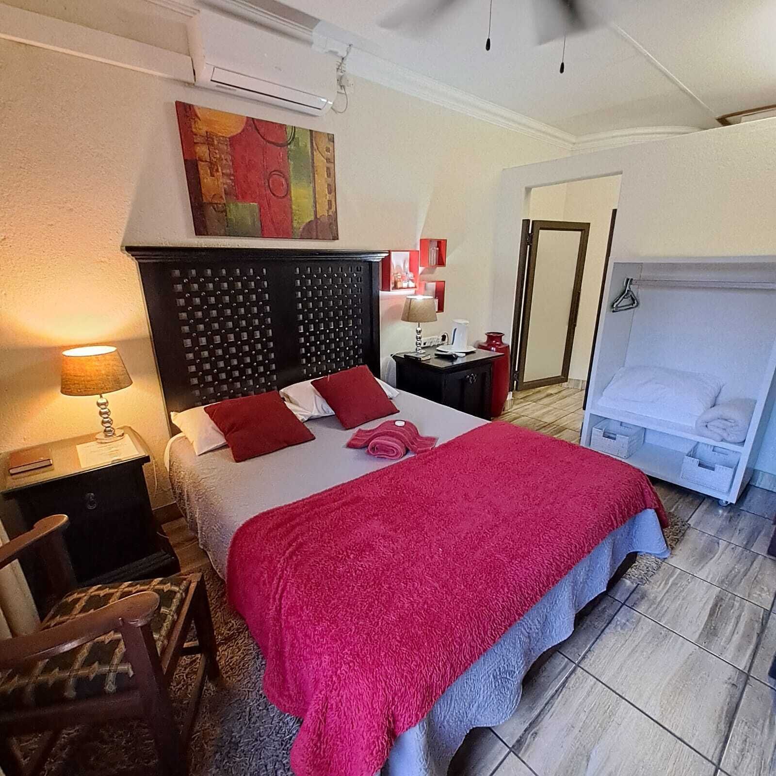 Ein Hotelzimmer mit einem Bett, einem Nachttisch, einer Lampe, einem Sessel, einem Schrank und einer Tür zu einem weiteren Raum.