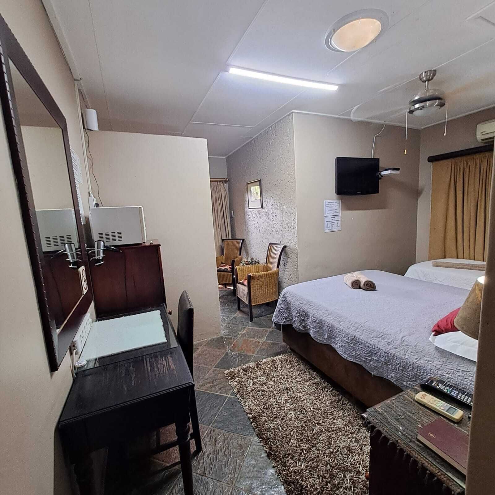 Habitación de hotel con cama, escritorio, silla, televisión y un baño visible al fondo.