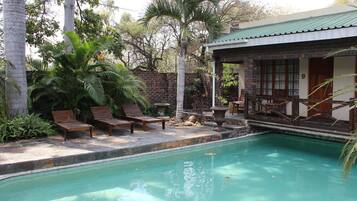A pool area with wooden lounge chairs, a brick wall, and a building with a green roof.