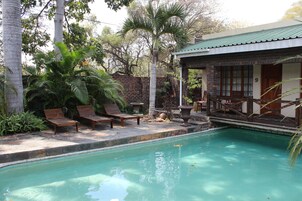 A pool area with wooden lounge chairs, a brick wall, and a building with a green roof.
