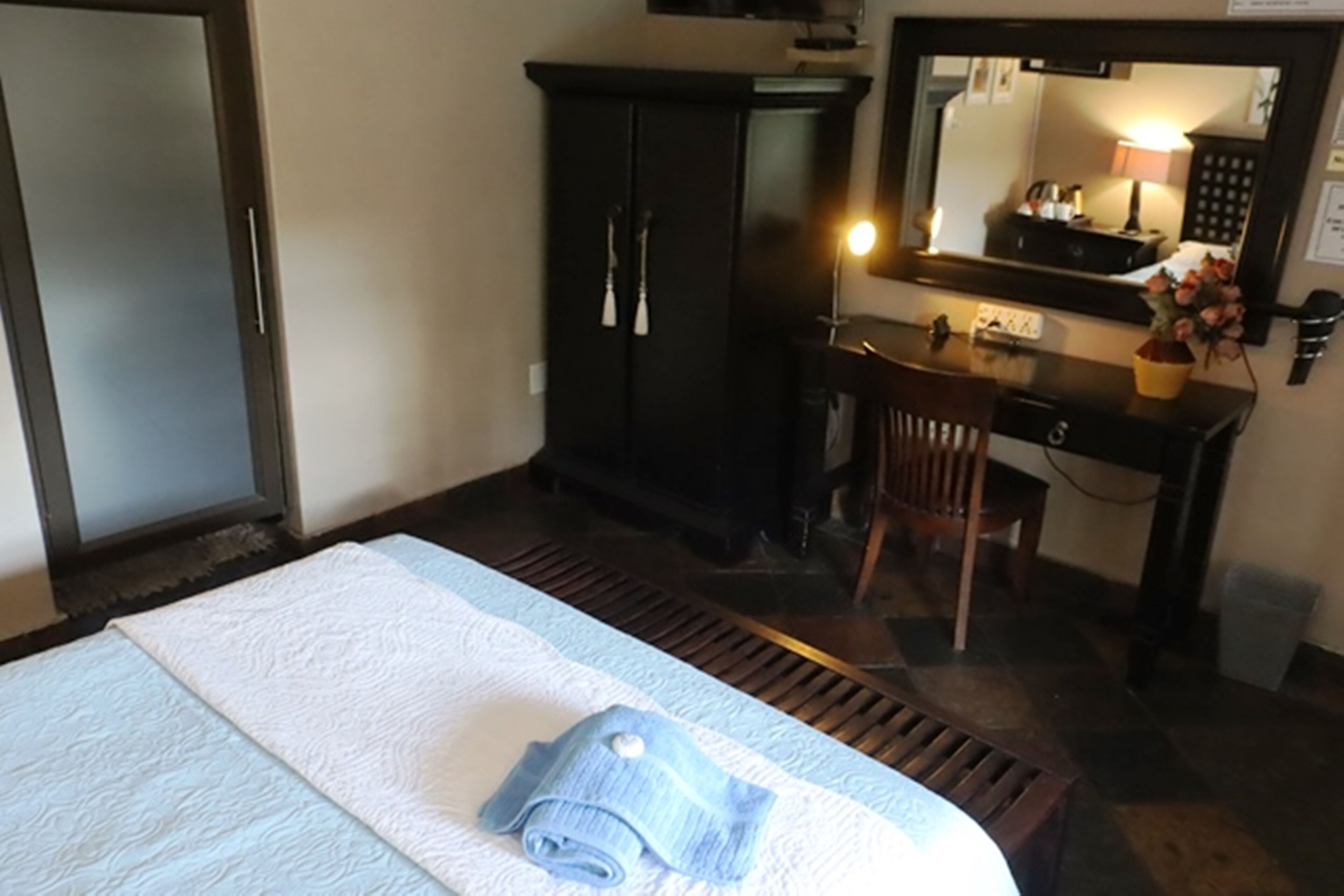 Una habitación de hotel con cama, escritorio, silla, armario y espejo.