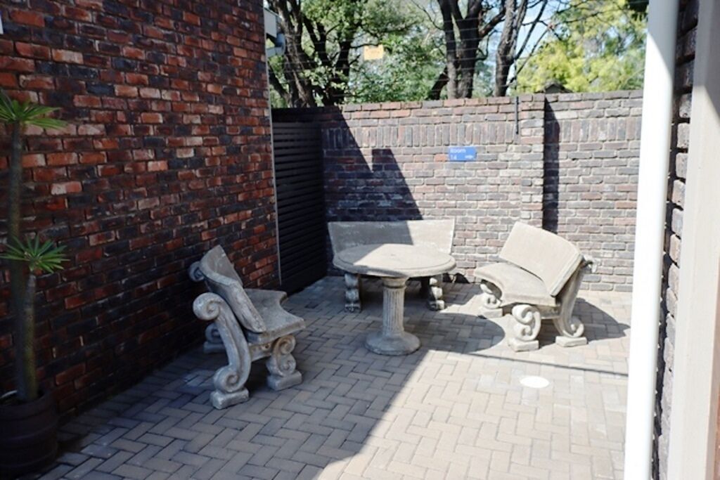 Un patio al aire libre con un muro de ladrillo, una puerta metálica y dos bancos de piedra.