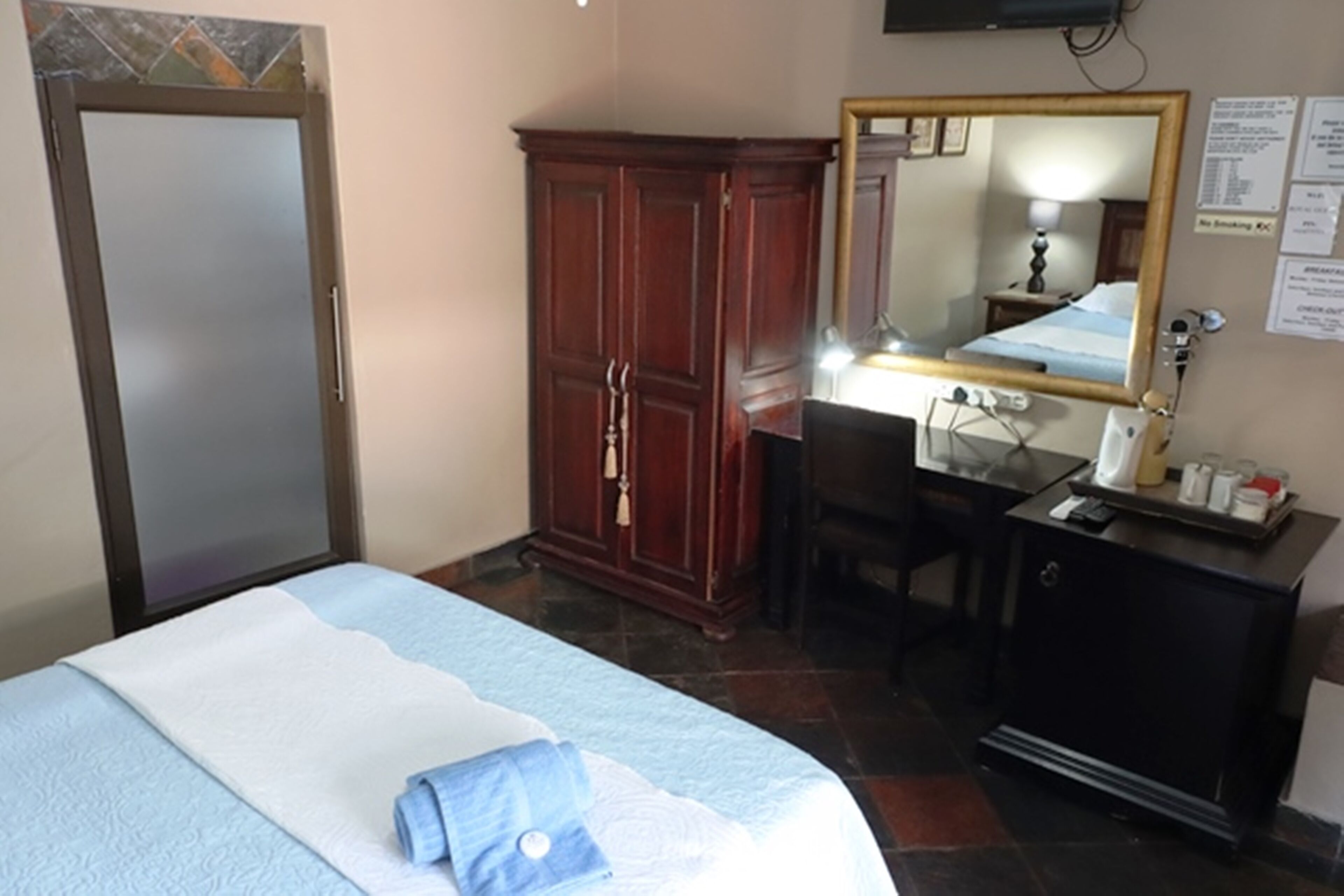 Habitación de hotel con cama, armario de madera, escritorio con silla, espejo y mesita de noche.