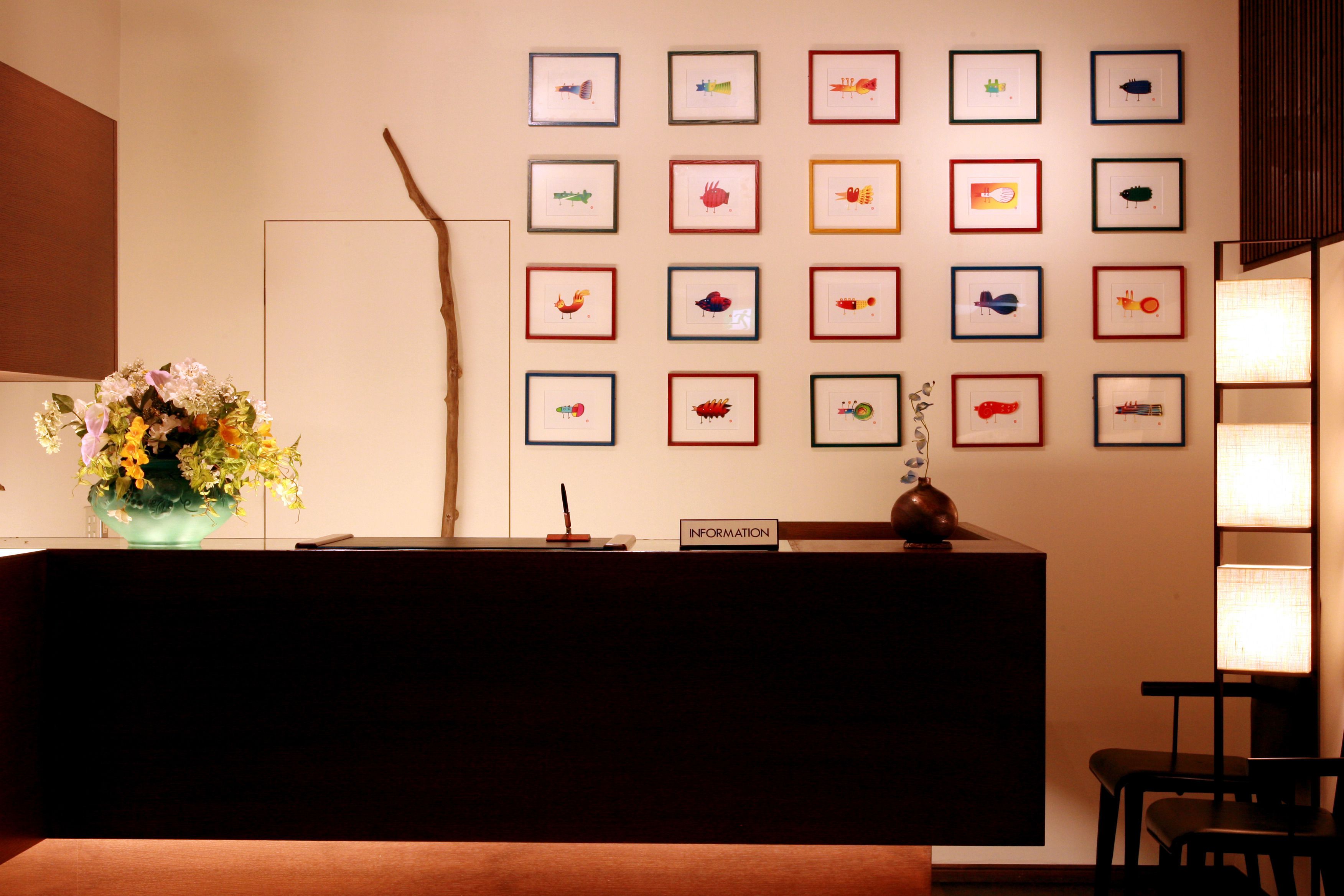 A reception desk with framed artwork on the wall, a vase of flowers, and a sign labeled "INFORMATION".