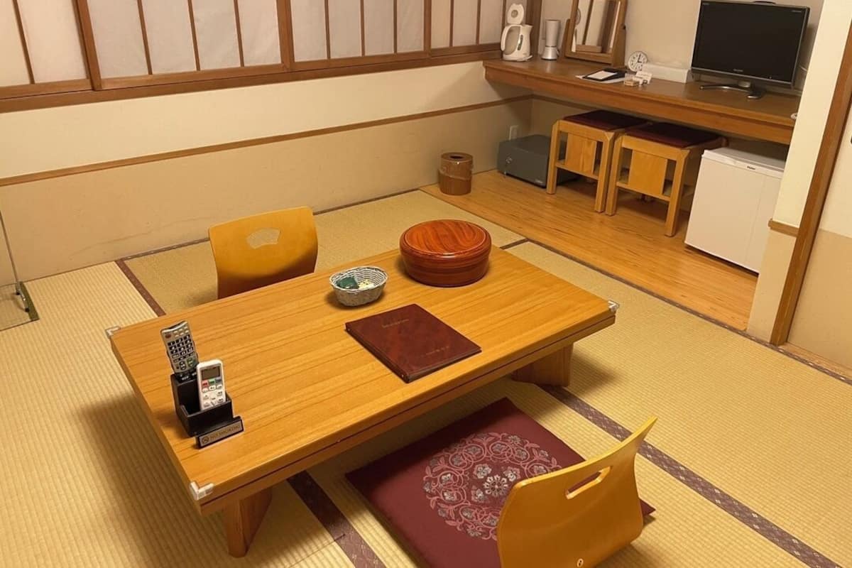 Una tradizionale stanza giapponese con pavimento in tatami, un tavolino in legno, una televisione e un piccolo frigorifero.