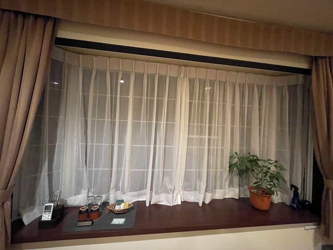 A window with sheer curtains, a potted plant, and a small table with a phone, glasses, and a tray.