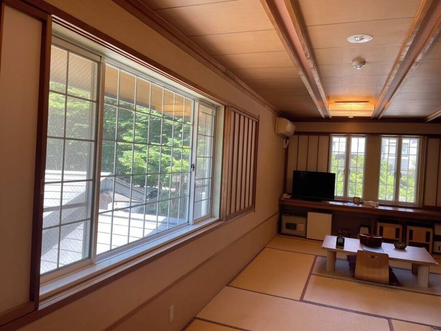 Una habitación japonesa tradicional con suelo de tatami, televisor y vistas a zonas verdes.