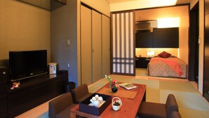 Habitación de hotel con televisor, una mesa de comedor con juego de té, cama y armario corredero.