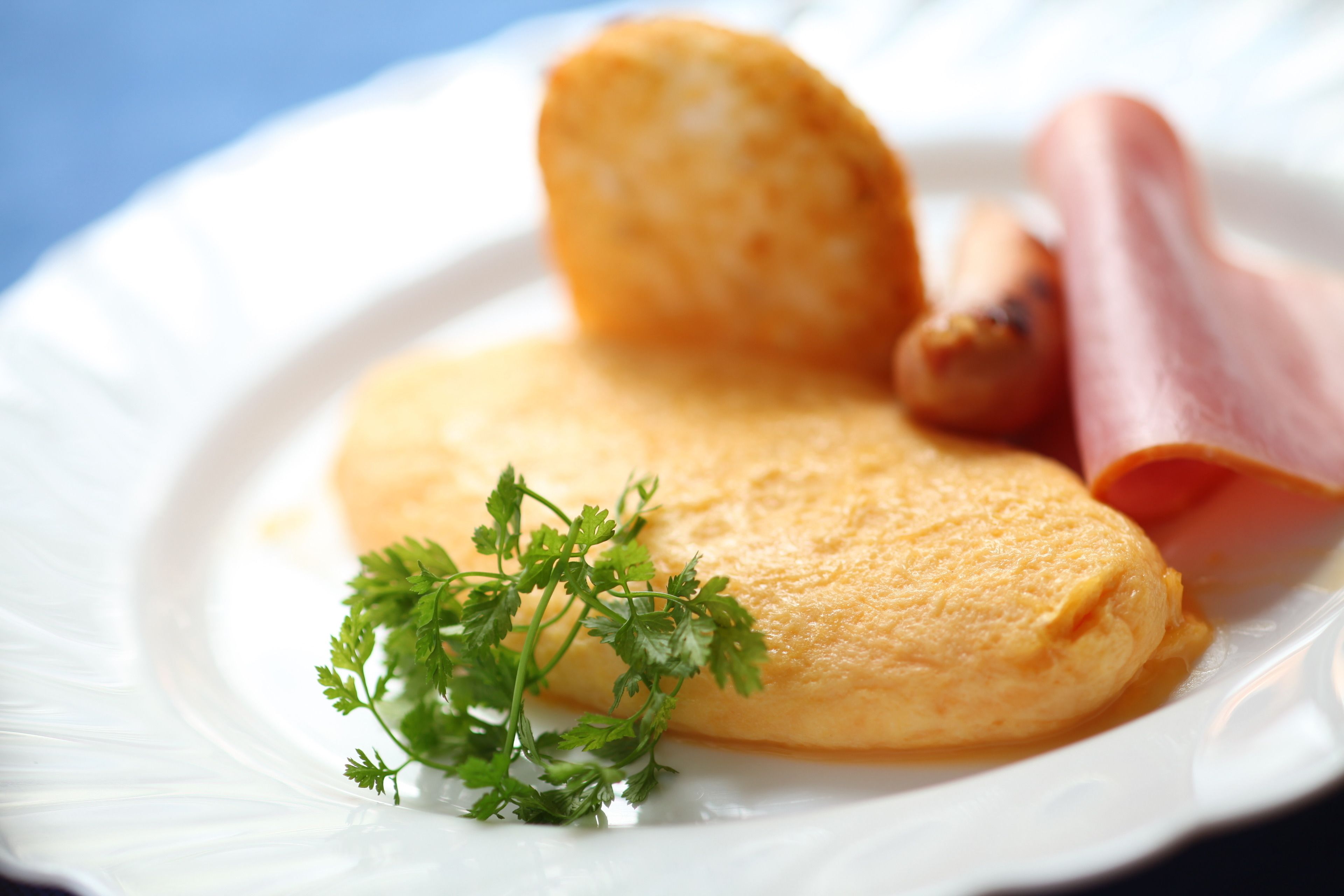 Um prato com uma omelete dobrada, uma fatia de presunto e um ramo de salsa.