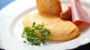Um prato com uma omelete dobrada, uma fatia de presunto e um ramo de salsa.