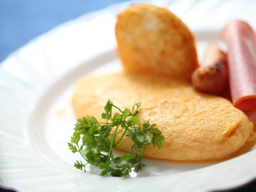 Um prato com uma omelete dobrada, uma fatia de presunto e um ramo de salsa.