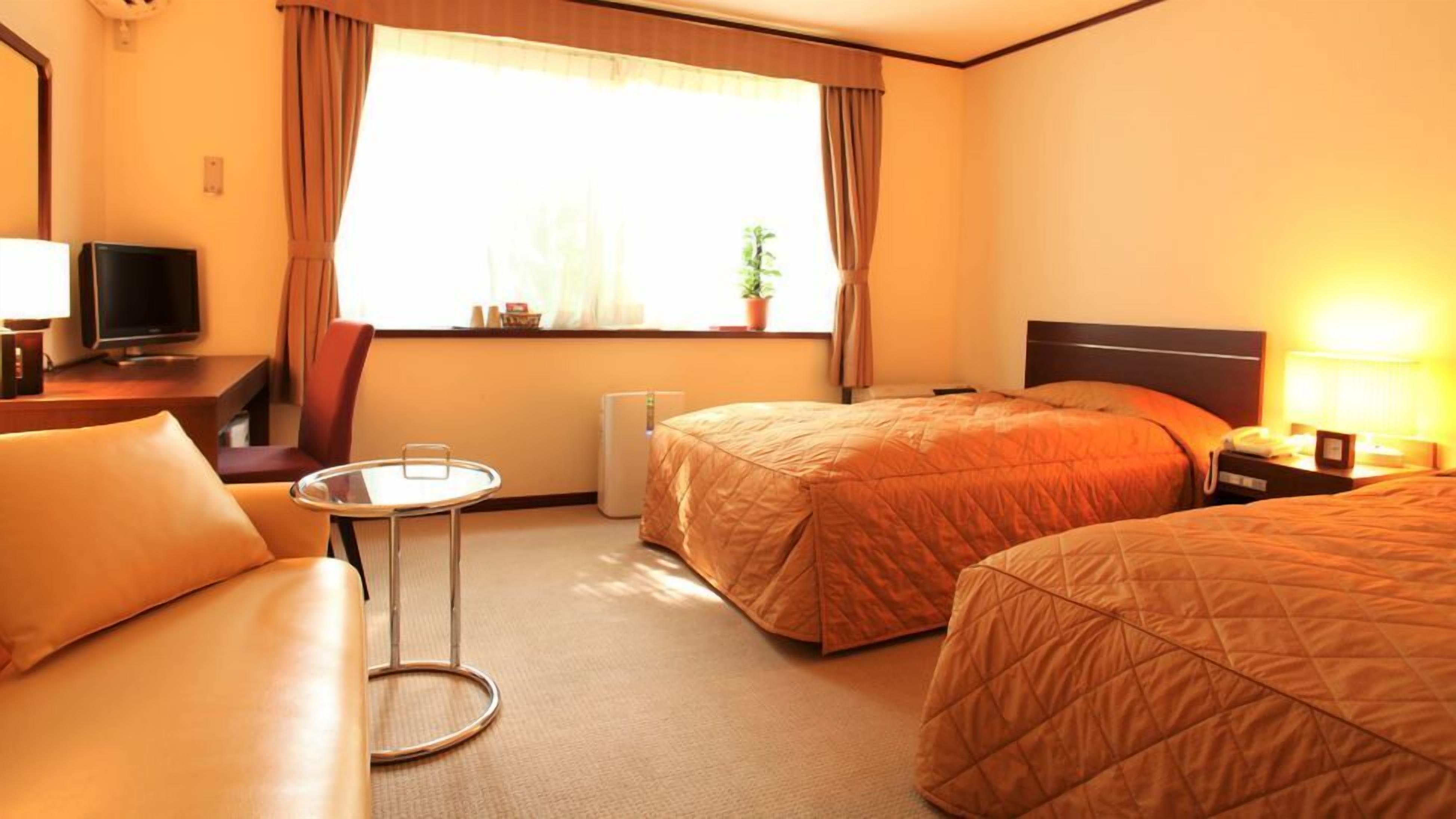 A hotel room with two beds, a small table, a TV, and a window with curtains.