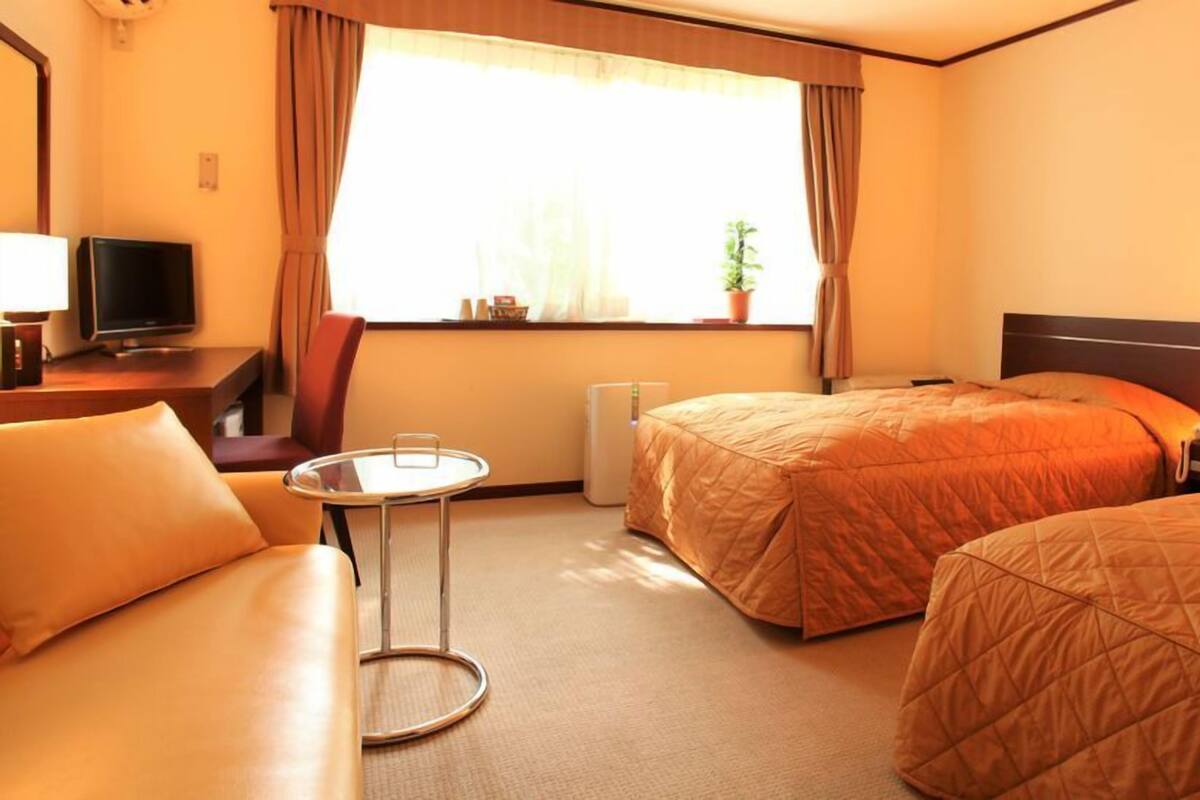 Una camera d'albergo con due letti, un tavolino, una televisione e una finestra con tende.