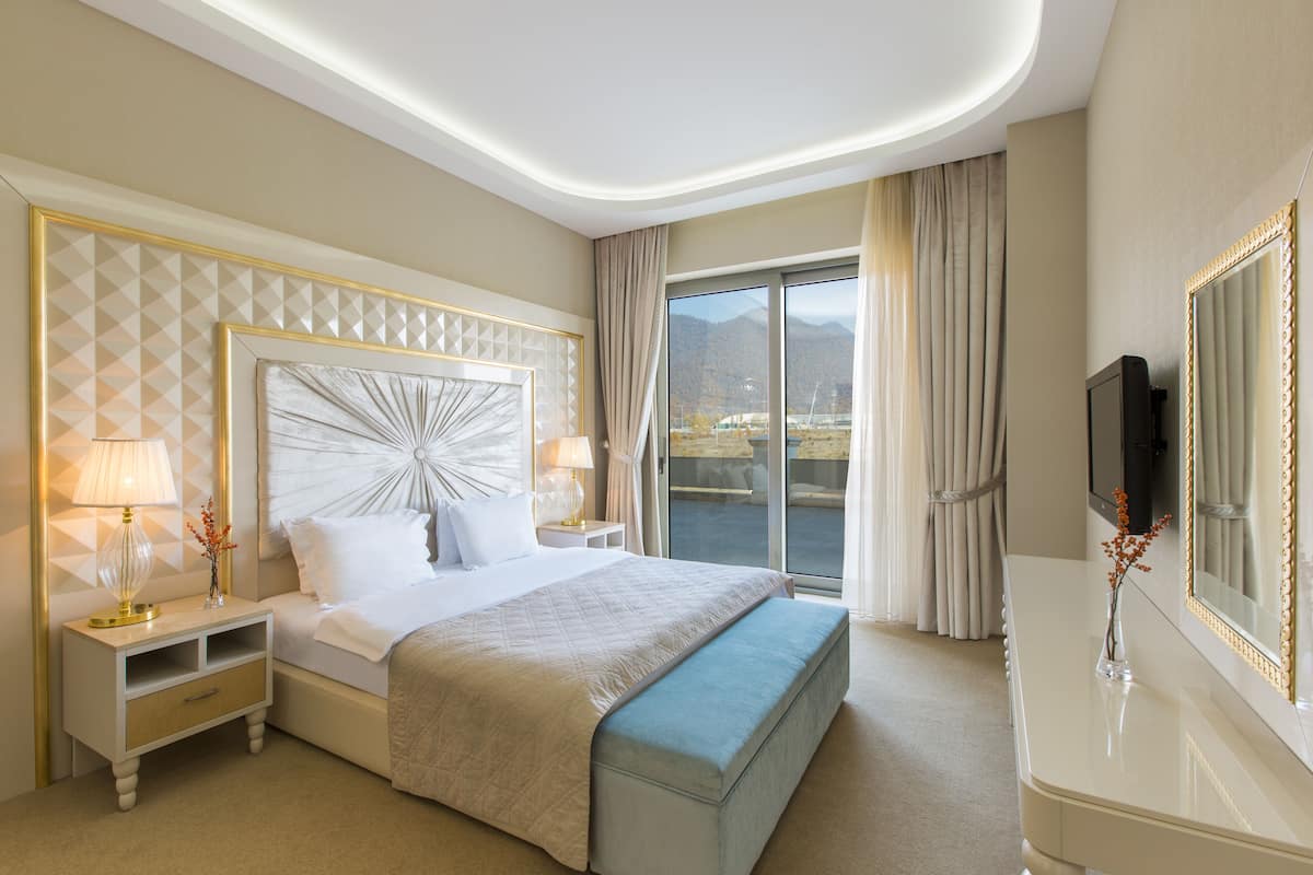 A hotel room with a large bed, a nightstand with a lamp, a dresser, and a large mirror.