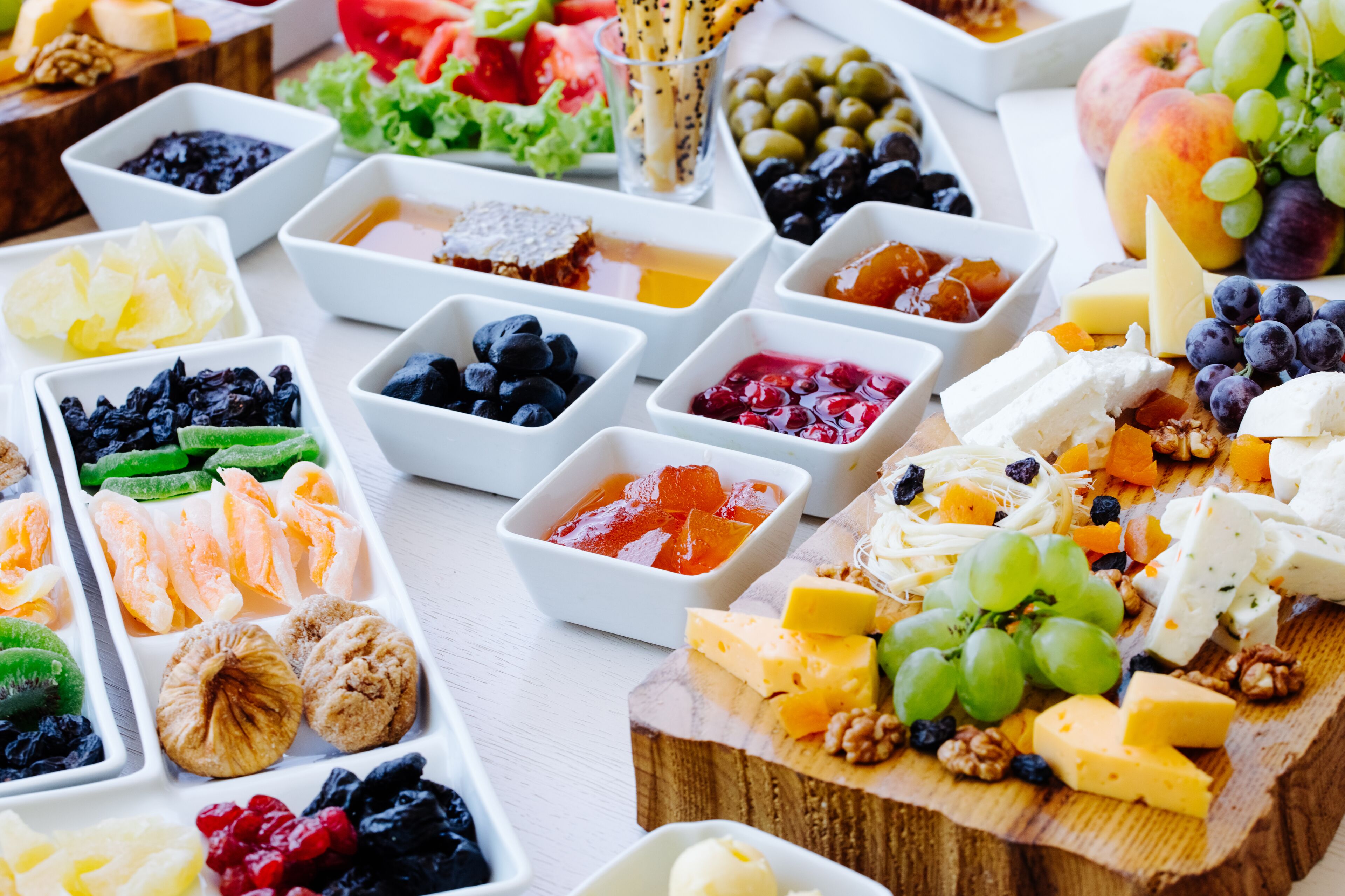 A variety of cheeses, fruits, and nuts arranged on a wooden board and in small bowls.