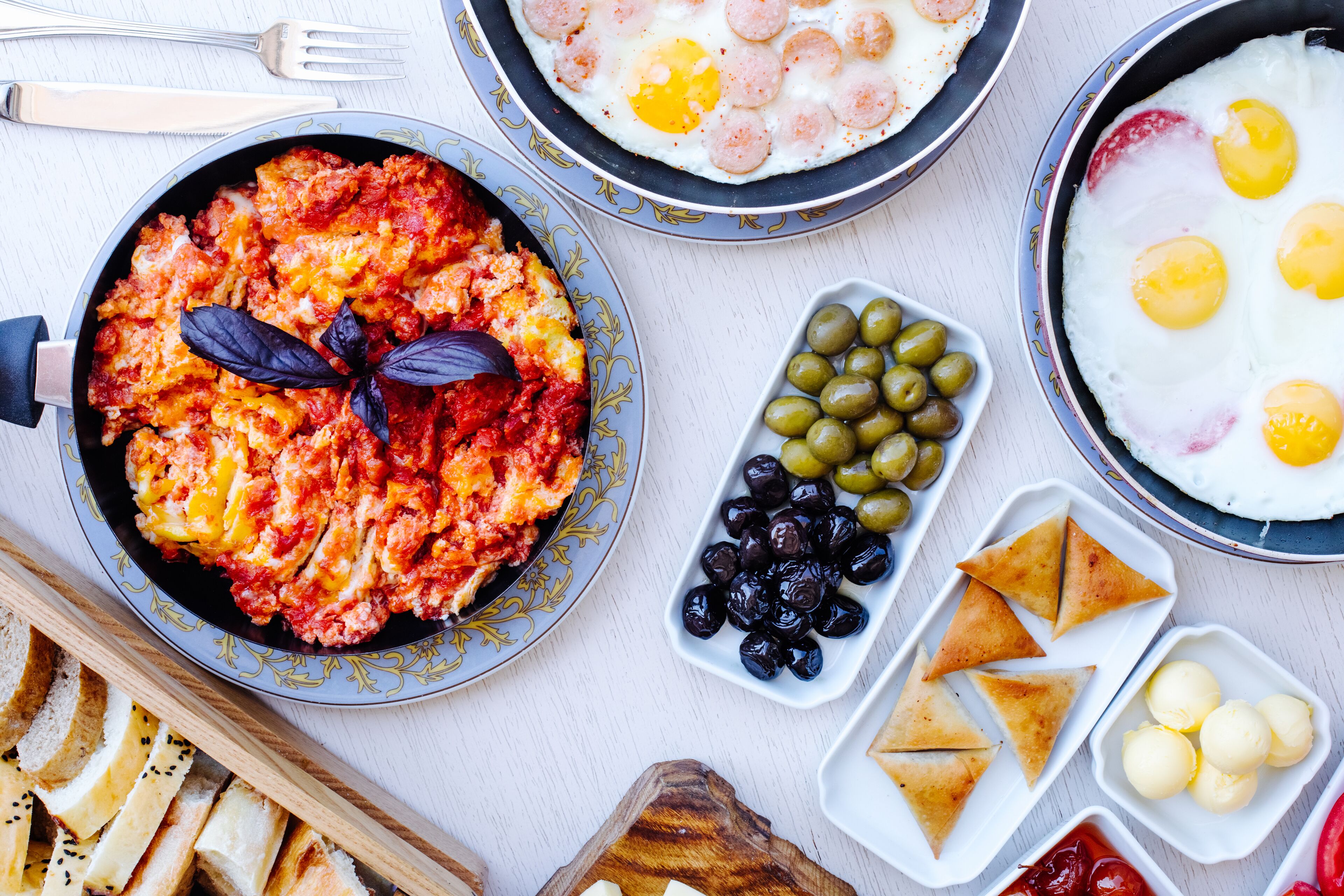 Un assortiment de mets pour le petit-déjeuner comprenant des œufs brouillés, un plat à base de tomates, des olives et du pain.