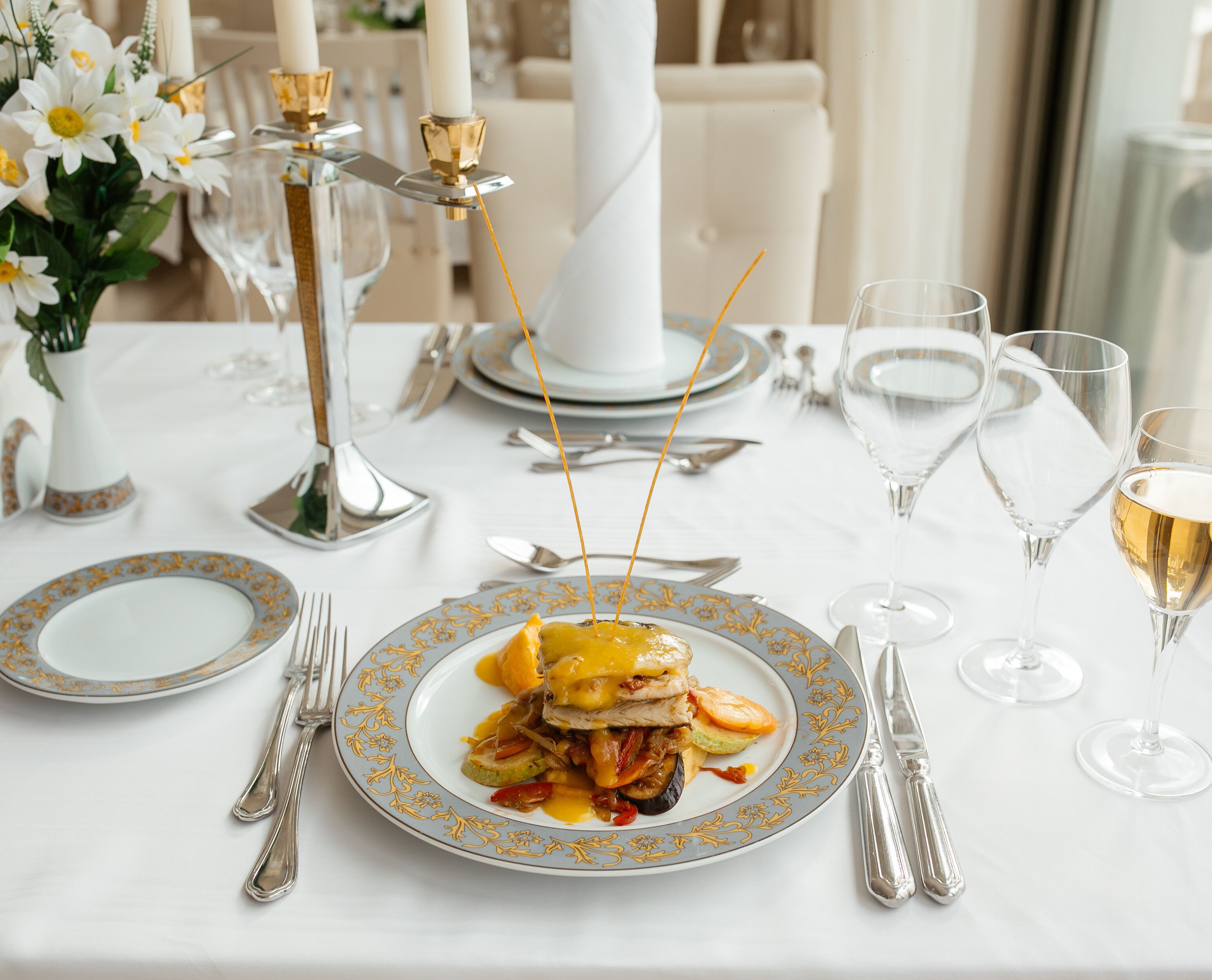 A formal dining table set with plates, cutlery, and glasses, featuring a centerpiece of flowers and candles.