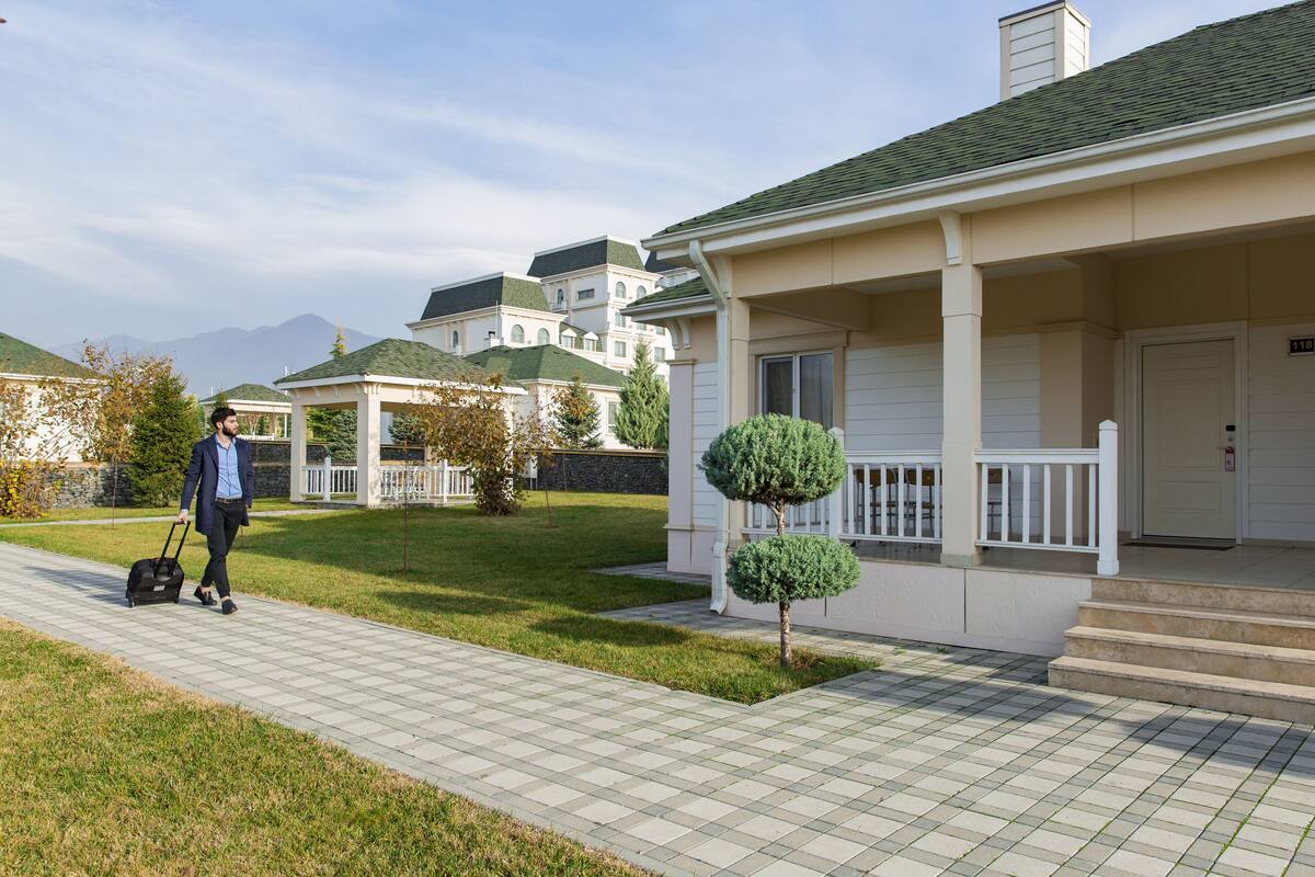A residential area with a house featuring a porch, a small tree, and a clear sky.