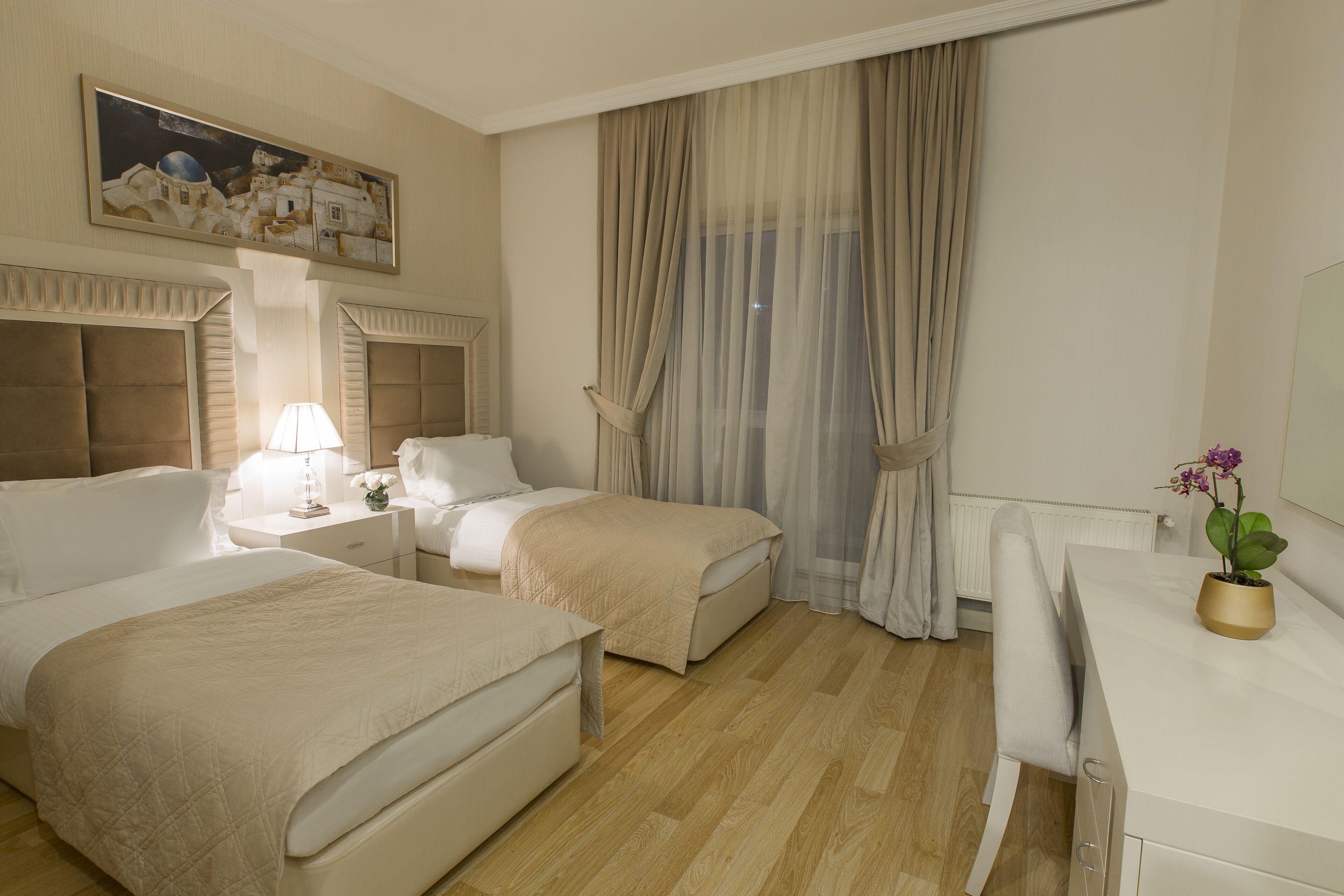 Habitación de hotel con dos camas, un escritorio, una lámpara y un cuadro en la pared.